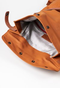 Bruine leren tas met een gevoerde binnenkant met een ruitpatroon, magnetische sluiting en een rode ritszak aan de binnenkant.