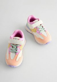 Des baskets colorées avec un mélange de matériaux blancs, roses, bleu clair et jaunes, dotées d'une semelle texturée et d'une sangle Velcro.