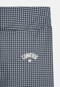 Marineblått houndstooth-mønster med hvit "Converse"-logo og stjernetillegg nær bunnen. Materialet ser teksturert og lett ut.