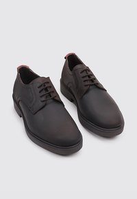 Zapatos de cuero marrón con una textura lisa, puntera redondeada, acentos de costura elevada en los lados y un diseño con cordones.