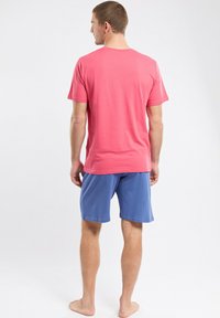 T-shirt rouge à manches courtes et shorts bleus. Tissu doux avec une coupe décontractée. Le T-shirt a un col rond et un style minimal.
