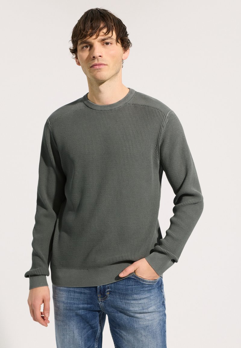 Pull gris à manches longues côtelé avec un col rond, doté d'un tissu texturé et de poignets ajustés, associé à un jean en denim bleu.