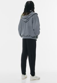 Hanorac oversized gri cu glugă ajustabilă și pantaloni de trening negri. Ținuta are pantaloni cu manșete și este completată cu adidași albi.
