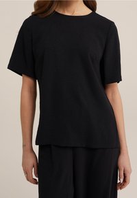 Černý krátký rukáv top s kulatým výstřihem, vyrobený z texturované tkaniny, s volným střihem a jednoduchým designem, v kombinaci s odpovídajícími kalhotami.