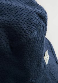 Cappello a secchiello blu navy realizzato in tessuto testurizzato con una superficie a motivo, caratterizzato da un piccolo tag con logo bianco sul lato.