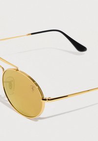 Στρογγυλά, χρυσά γυαλιά ηλίου με φακούς κίτρινου χρώματος. Λεπτό χρυσό πλαίσιο με μαύρες άκρες στα μπράτσα. Διαθέτουν διακριτικό λογότυπο στον φακό.