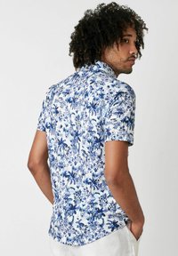 Kurzarmhemd in Weiß mit blauem Blumenmuster. Hat einen Kragen, eine durchgehende Knopfleiste und einen abgerundeten Saum. Aus weichem Stoff.