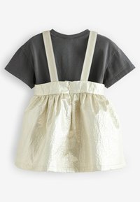 Grå t-shirt med kort ärm och en metallisk guldig, texturerad kjol med justerbara band; bakifrån syns knapp- och rynkdetaljer.