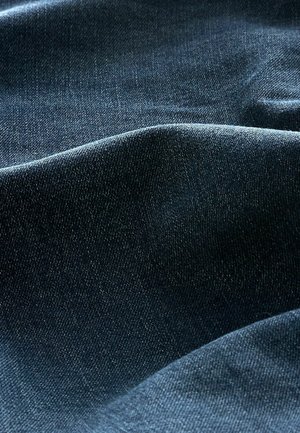 Tela de denim azul oscuro con una textura de tejido visible y suaves pliegues que crean sombras y luces suaves.