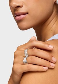 Anillo de plata con un patrón ondulado, utilizado en los dedos. Superficie lisa, acabado brillante, diseño ligero, que complementa el tono natural de la piel.