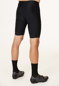 Schwarze Radshorts mit gepolsterter Sitzfläche, glatter Textur, mittellange Länge bis zum Oberschenkel, kombiniert mit schwarzen Sportstrümpfen und schwarzen Schuhen.