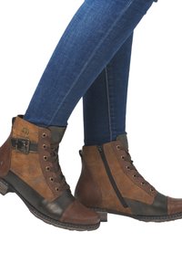 Bottines marron et noires avec une tige texturée, des lacets, une fermeture éclair sur le côté et un talon carré. Associées à un jean skinny bleu foncé.