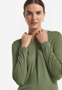 Olivgrön tröja i mjukt material, med långa ärmar och rund halsringning samt ribbade muddarna. Slät textur med minimal detaljering.