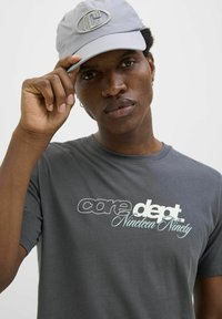 Grå kortærmet t-shirt med hvid og lyseblå tekst, der står "core dept. Nineteen Ninety." En grå kasket med logo-udsmykning.