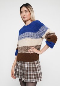 Strickpullover mit horizontalen Streifen in Blau, Beige und Braun mit einer strukturierten Oberfläche. Kombiniert mit einem karierter, plissierter Rock.