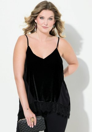 Zwarte camisole met dunne spaghettibandjes, gemaakt van fluweelachtige stof, met kant langs de zoom. Gestyled met losse zwarte broek en een clutch.