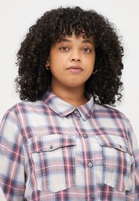 Cămașă cu nasturi din material ușor, cu un model tartan în culori albastre, roz și alb. Include două buzunare pe piept și guler.