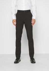 Fekete elegáns nadrág, slim fit szabással, sima anyaggal, övhurkokkal és hagyományos elülső gombos záródással, fényes fekete cipőkkel párosítva.