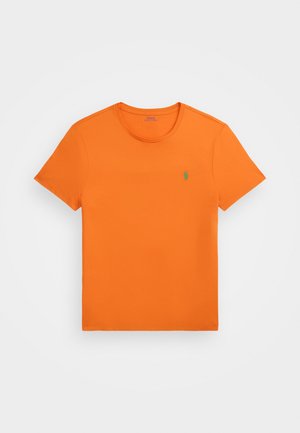 T-shirt orange vif en coton, avec un col rond, des manches courtes et un petit logo vert sur la poitrine gauche. Texture lisse.