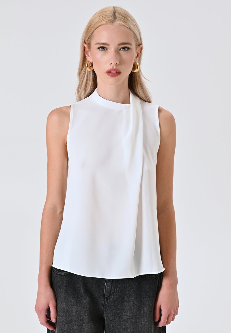 Blusa bianca senza maniche con collo alto e accento drappeggiato. Realizzata in un tessuto leggero e liscio, presenta una vestibilità rilassata.