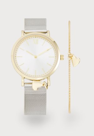 Montre-bracelet en or et argent avec un bracelet en maille et un pendentif en forme de cœur, associée à un bracelet en or avec un pendentif cœur assorti.
