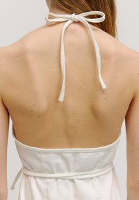 Weißes, ärmelloses Kleid mit tiefem Rückenausschnitt und Stoffband am Hals. Das Material wirkt glatt und leicht und zeigt eine taillierte Silhouette.