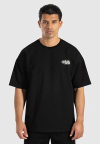 Camiseta de algodón negra con un corte holgado, con mangas cortas y un pequeño logo blanco en el pecho. Textura suave, diseño casual.