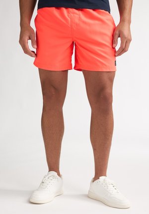 Shorts de bain orange néon en matériau léger, offrant une coupe décontractée. Agrémentés d'une petite étiquette de marque sur le côté.