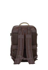 Sac à dos en tissu marron avec deux bretelles rembourrées, une poignée de transport supérieure, des poches latérales en maille et des boucles de harnais réglables.