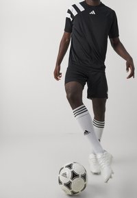 Černé sportovní dres s bílými pruhy na ramenou, černé šortky, bílé ponožky se třemi černými pruhy a černo-bílý fotbal.