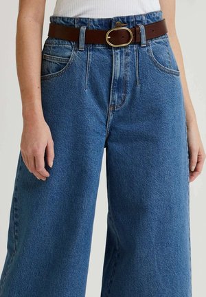 Pantalones de mezclilla anchos de color azul con cintura alta, combinados con un cinturón de cuero marrón que presenta una hebilla ovalada en tono dorado.