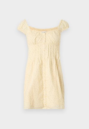 Gul kort kjole med lite blomstermønster, korte puffermet, knappestolpe foran og folder på høyre side under bysten.