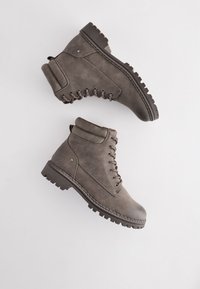 Botines grises hasta el tobillo con un acabado texturizado, cordones en la parte delantera, cuello acolchado y suela de goma resistente con surcos profundos para una mejor tracción.