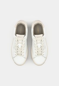 Sneakers bianchi in pelle con accenti in suede beige, lacci piatti e suole in gomma crema. Presentano il nome del marchio impresso sulla linguetta.