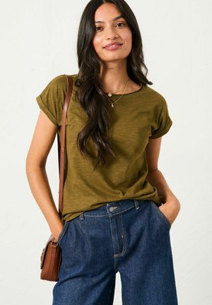 Olive green short-sleeve t-shirt with rolled cuffs, paired with blue denim wide-leg pants. Model holds a brown crossbody bag.