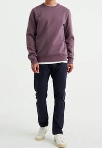 Lila sweatshirt med rund hals och ribbade ärmar, lager-på-lager över en vit skjorta. Matchas med mörka byxor och vita sneakers.