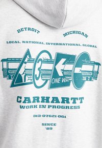 Gray sweatshirt featuring teal graphics, including road signs and text. Text includes "Carhartt," "Work in Progress," and location details.