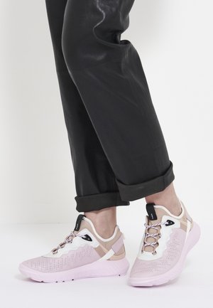 Person wearing cuffed black pants and light pink athletic sneakers with white and beige accents standing on a white surface.