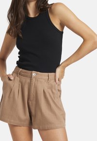 Mustat ribbed-hihattomat topit yhdistettynä beigeihin laskostettuihin shortseihin, joissa on napitus ja sivutaskut. Pehmeä kangas ja rento istuvuus.