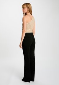 Top beige monospalla con paillettes abbinato a pantaloni neri a vita alta, che mettono in risalto una silhouette aderente e una texture liscia.