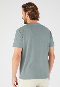Camiseta corta de manga gris con una superficie texturizada, escote redondo y un ajuste relajado, vista desde la parte posterior.
