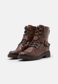 Bottes courtes marron avec un motif croco texturé, devant lacé, ferrures métalliques, fermeture éclair latérale et semelle épaisse. Dotées d'une bride avec boucle en accent.