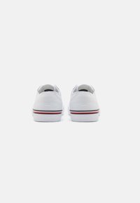 Weiße Sneakers mit einem Low-Top-Design, glatter Textur, kontrastierender schwarzer Umrandung und roten Akzenten an der Sohle. Ansicht von hinten, die die Nähdetails hervorhebt.