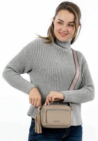 Beige kožená kabelka přes rameno se zipovým uzávěrem a třásňovými akcenty; obdélníkový tvar, měkká textura a nastavitelné ucho.