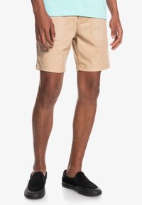 Beige shorts i slitstarkt tyg med två bakfickor, rak skärning och fållade innerbensömmar. Bärs med svarta slip-on skor.