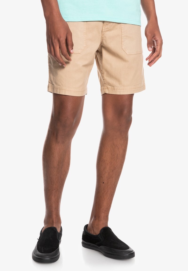 Beige shorts i slitstarkt tyg med två bakfickor, rak skärning och fållade innerbensömmar. Bärs med svarta slip-on skor.