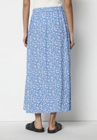 Modrá květinová midi sukně s elastickým pasem, se vzorem bílých květů, vyrobená z lehkého materiálu, a v kombinaci s černými sandály.