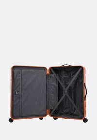 Tvrdý skořepinový oranžový kufr s černým vnitřkem, vybavený kapsou na zip, křížovými popruhy a hladce se točícími kolečky.