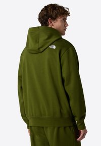 Olijfgroene hoodie met een relaxte pasvorm, geribbelde boorden en zoom; heeft een klein wit logo op de achterkant. Gemaakt van zachte stof.