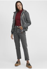 Gray hooded jacket with white zippers, maroon ribbed sweater, gray jeans, and black and tan patterned shoes. Casual fit and unembellished design.